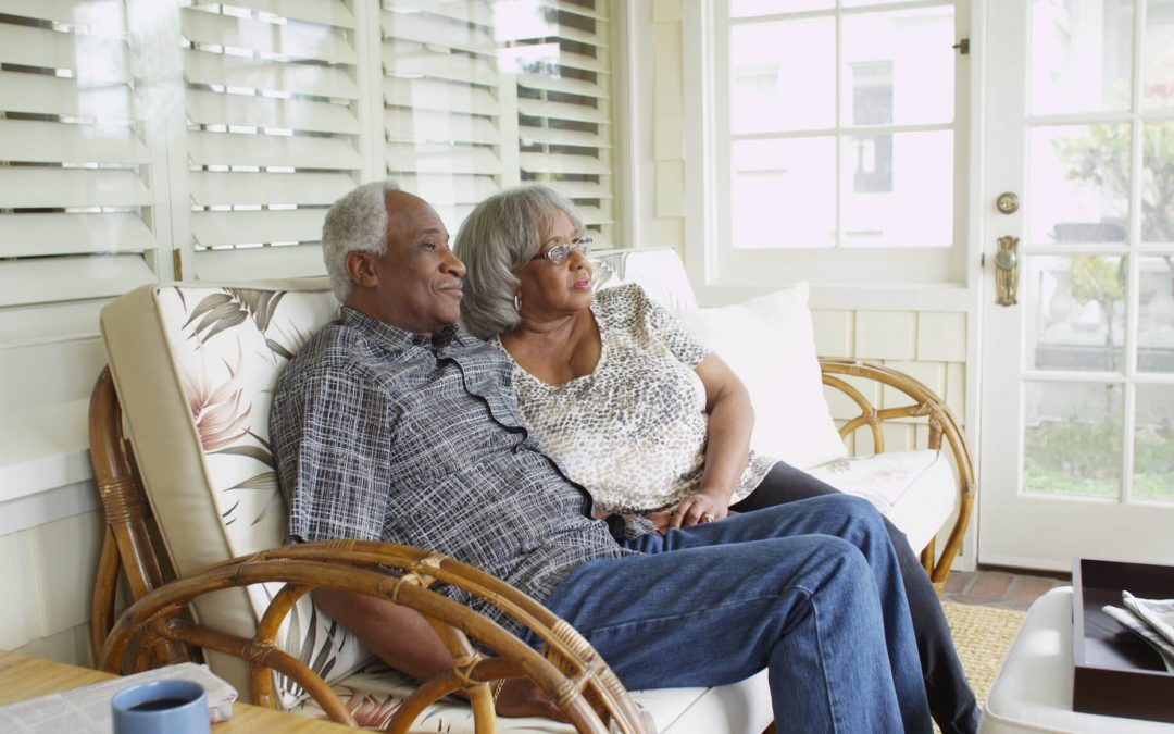 Older black couple, sitting on a porch swing looking outside and smiling.